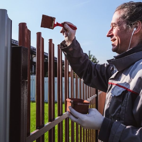 a-man-paints-an-iron-fence-in-the-garden-and-liste-2023-11-27-04-56-57-utc